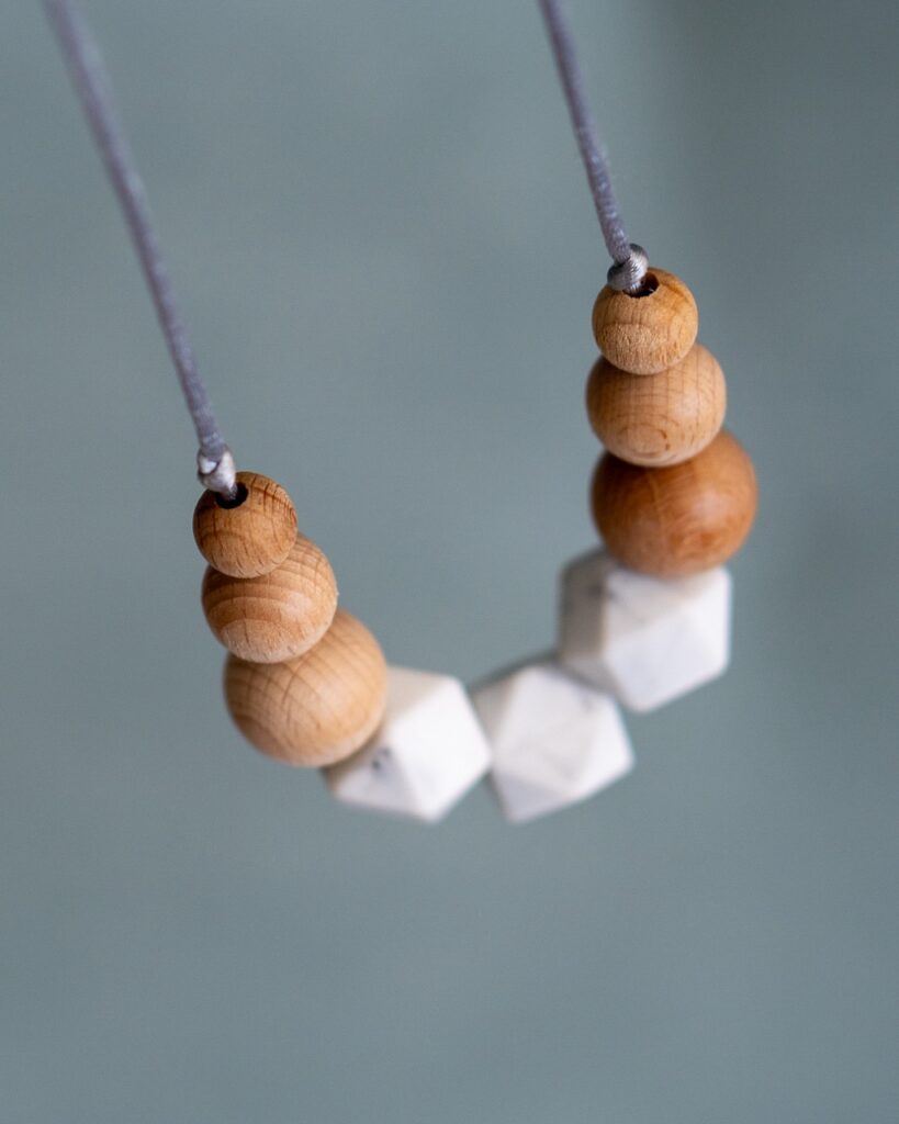 Collar de lactancia Sensory Lulumoon modelo Nórdico con piezas de mármol y madera sobre fondo verde.