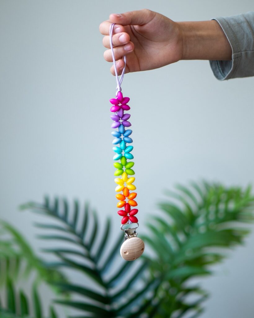 Chupetero de silicona con diseño de estrellas en colores del arcoíris y clip de madera de Lulumoon.