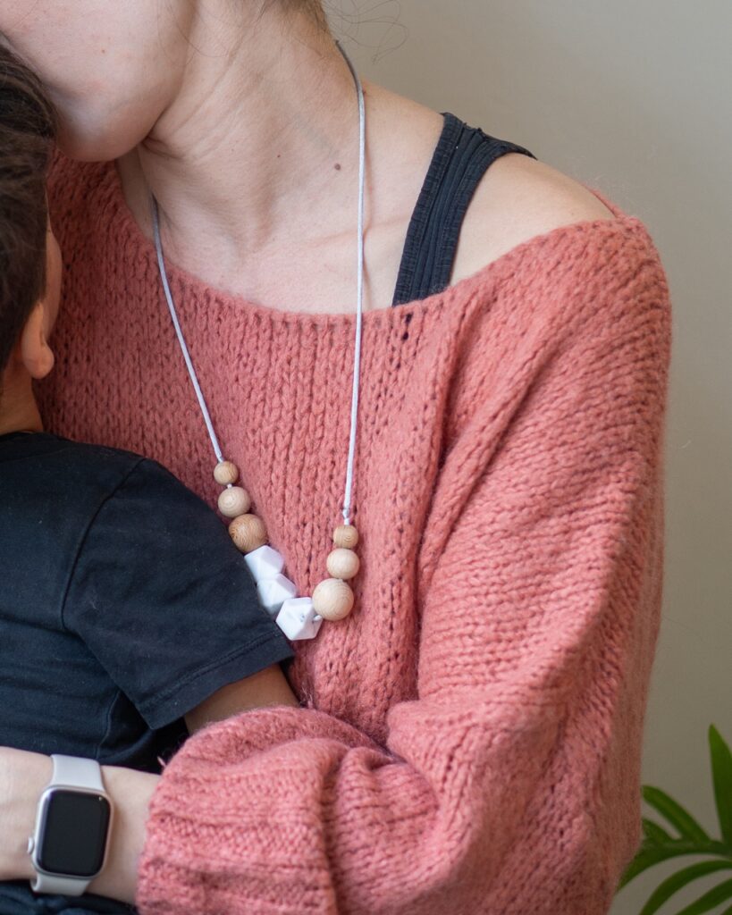 Collar de lactancia Sensory Lulumoon modelo Nórdico con piezas de mármol y madera sobre fondo verde.