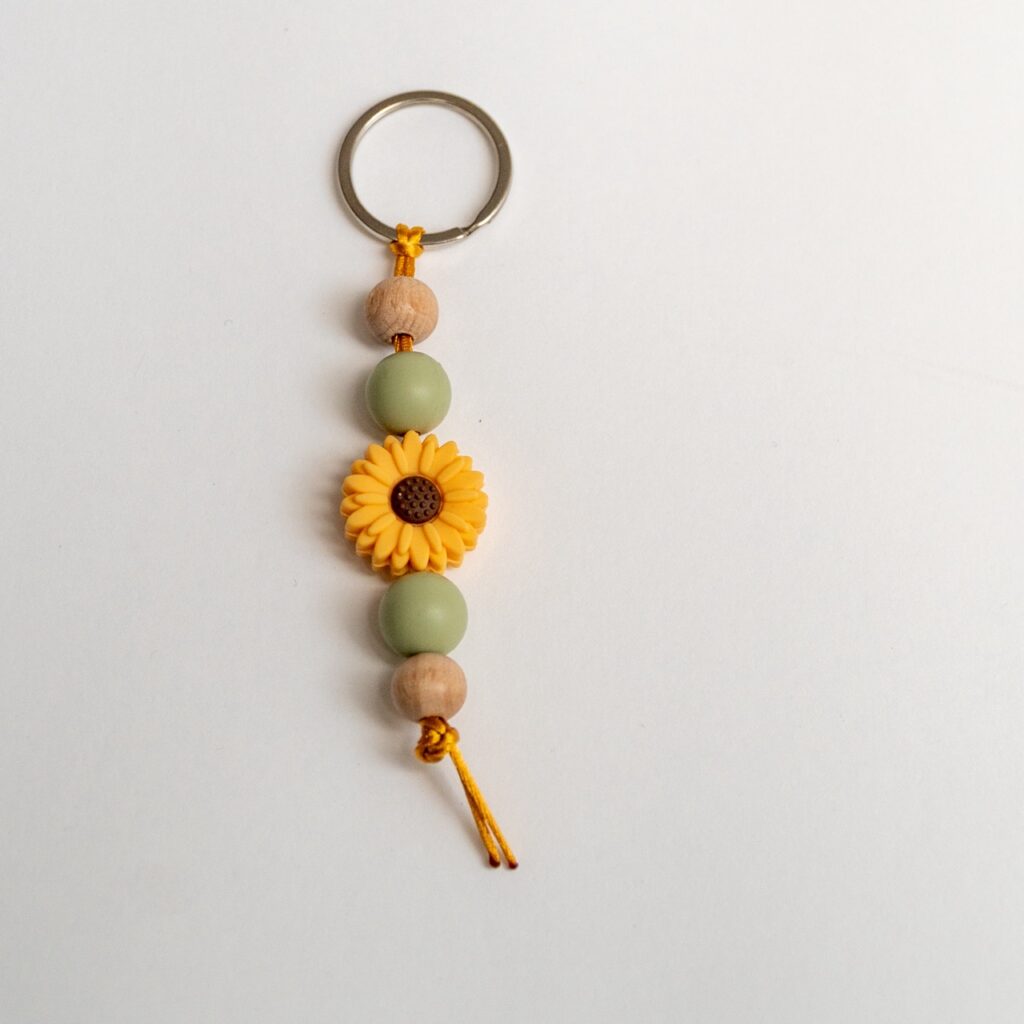 Llavero Lulumoon modelo Girasol con silicona amarilla, bolas verde oliva y madera de haya.