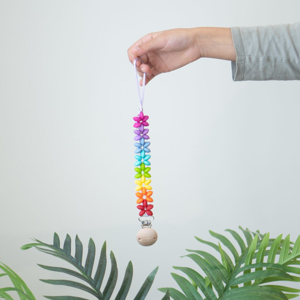Chupetero de silicona con diseño de estrellas en colores del arcoíris y clip de madera de Lulumoon.