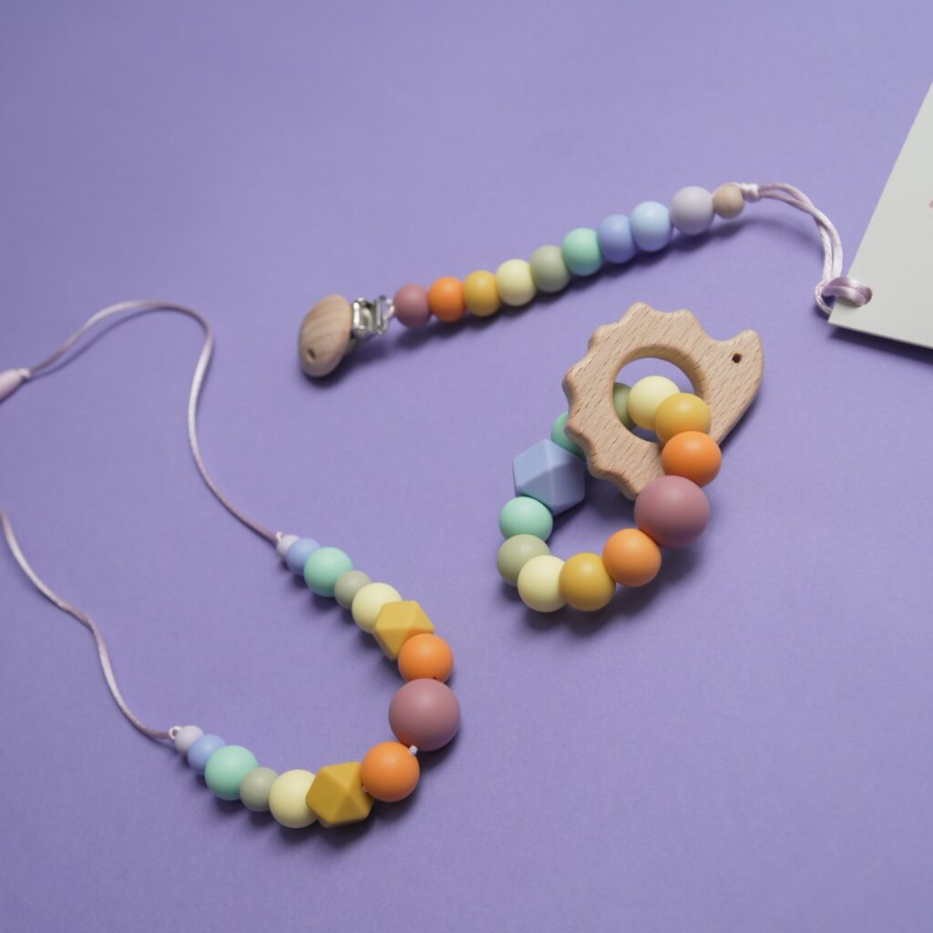 Conjunto de regalo para bebé con chupetero, mordedor de erizo y collar de apego en tonos arcoíris de Lulumoon.